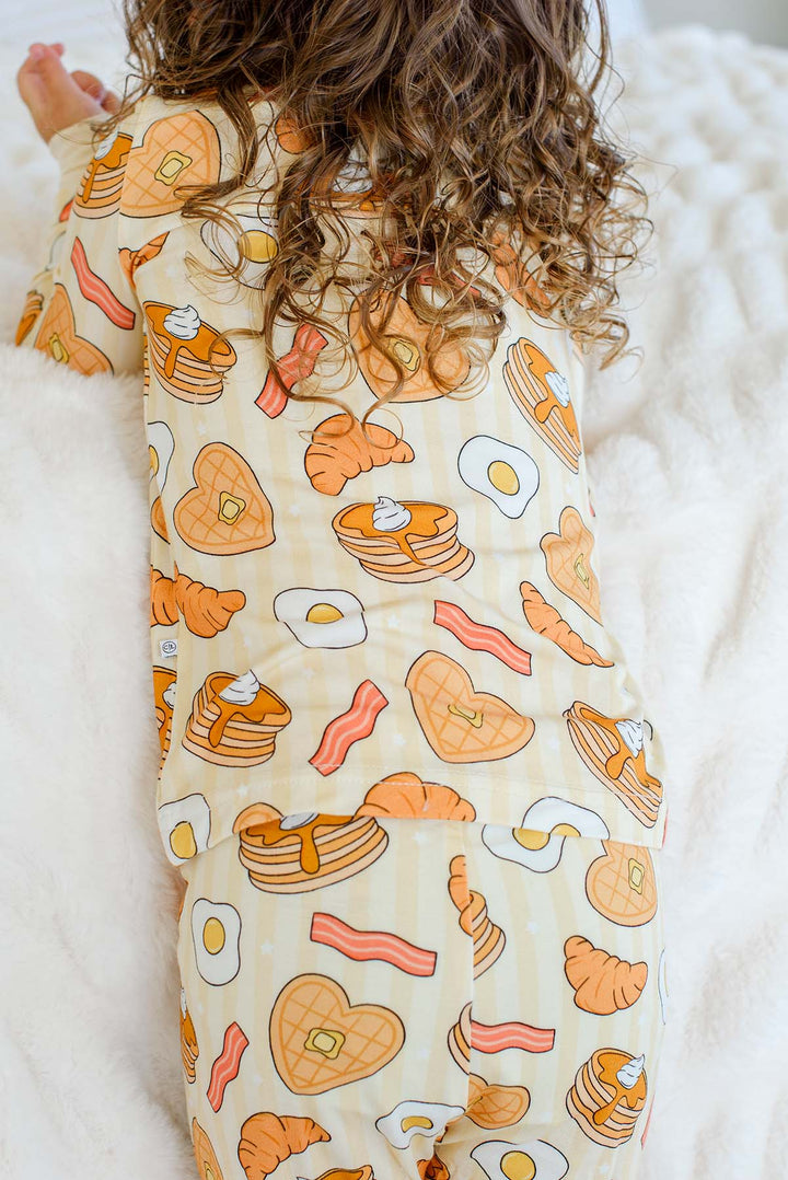 Back view of toddler in Caden Lane I Love You A Brunch two-piece pajamas, close-up of breakfast-themed print
