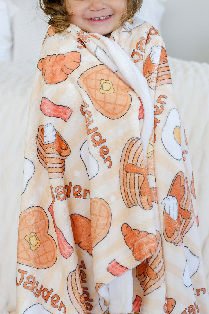 Close-up of toddler wrapped in Caden Lane personalized "Jayden" plush blanket, showing print and plush texture