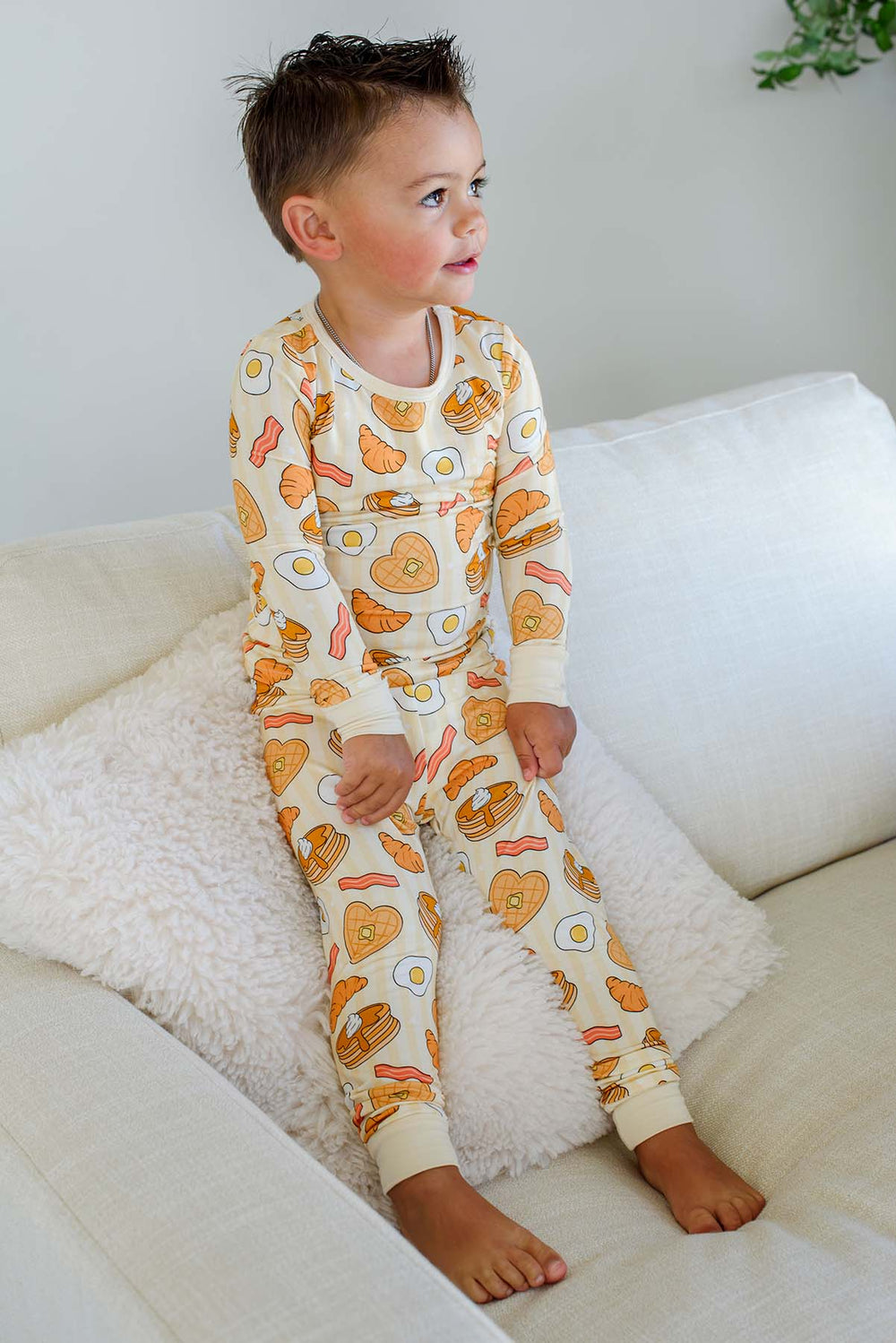 Toddler boy sitting on a couch wearing Caden Lane I Love You A Brunch long-sleeve pajama set