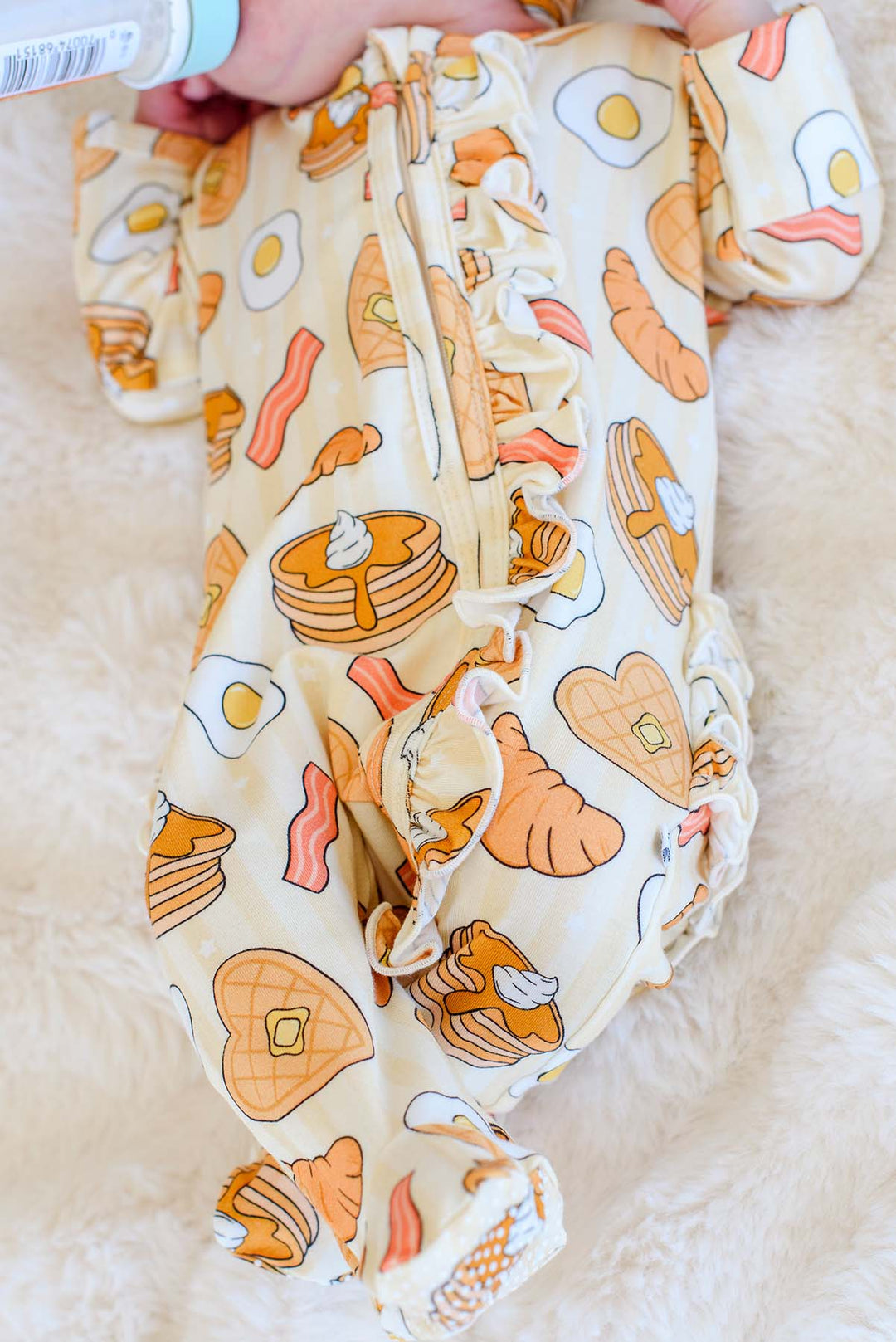 Close-up of Caden Lane I Love You A Brunch footie's zipper and ruffle trim on a newborn