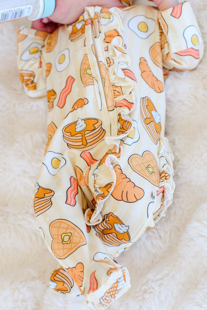 Close-up of Caden Lane I Love You A Brunch footie's zipper and ruffle trim on a newborn