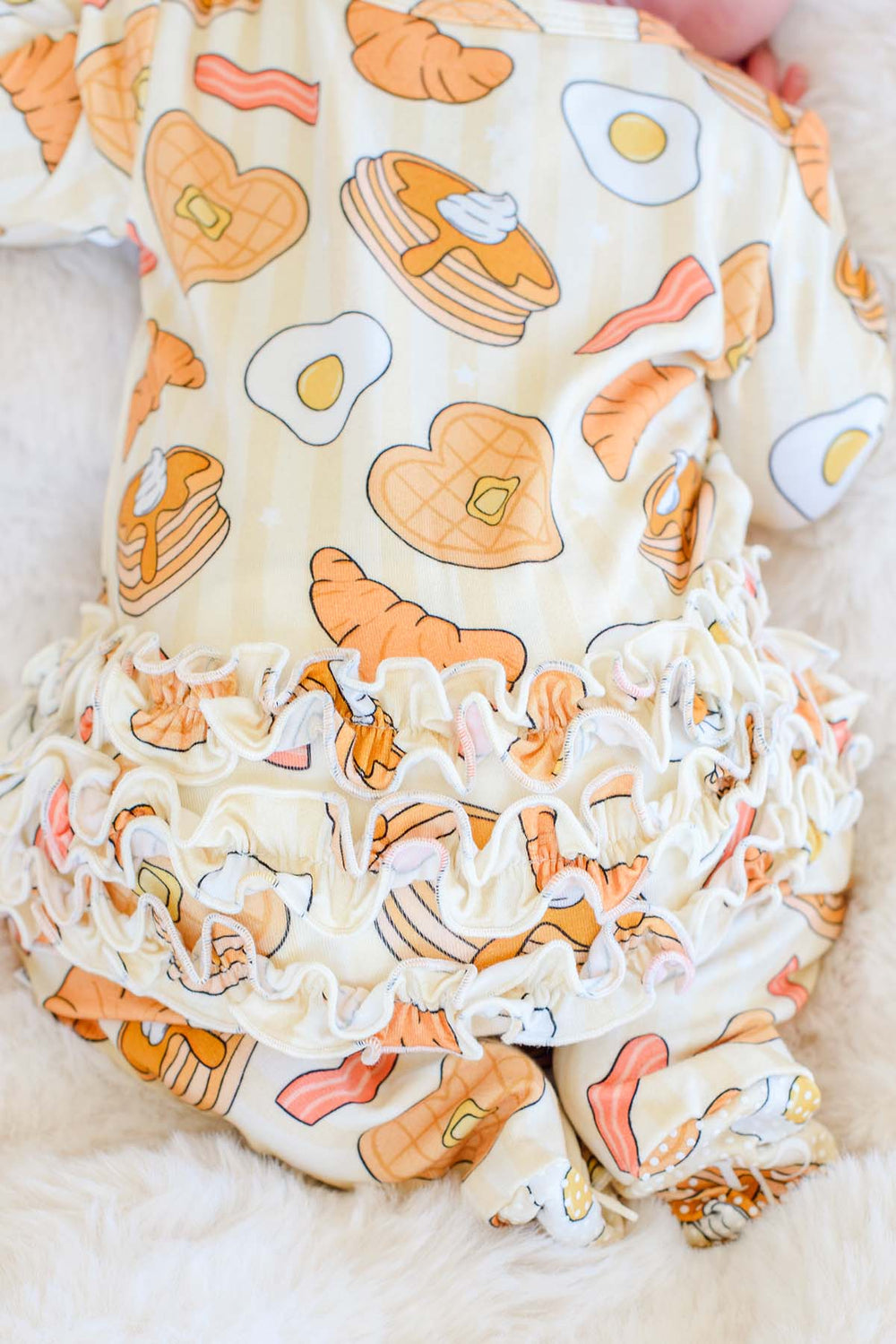 Close-up of ruffle trim and breakfast print on Caden Lane I Love You A Brunch footie, back view
