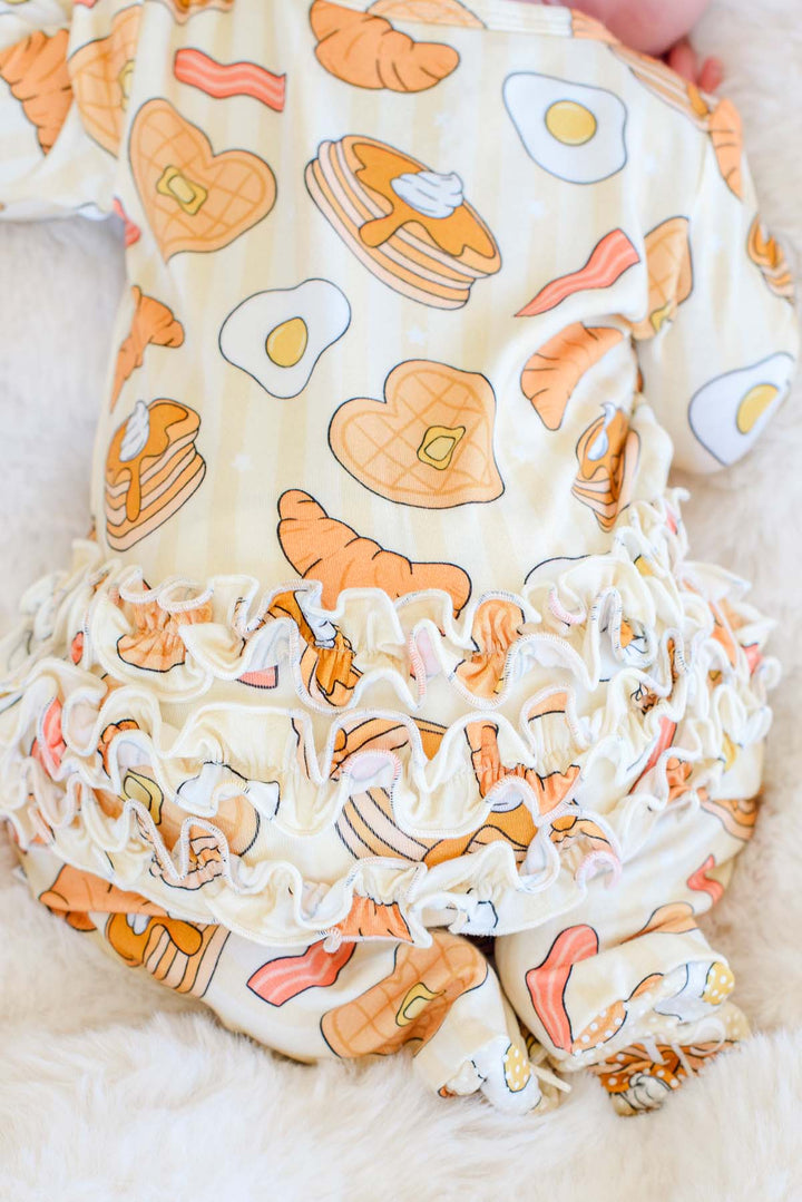 Close-up of ruffle trim and breakfast print on Caden Lane I Love You A Brunch footie, back view