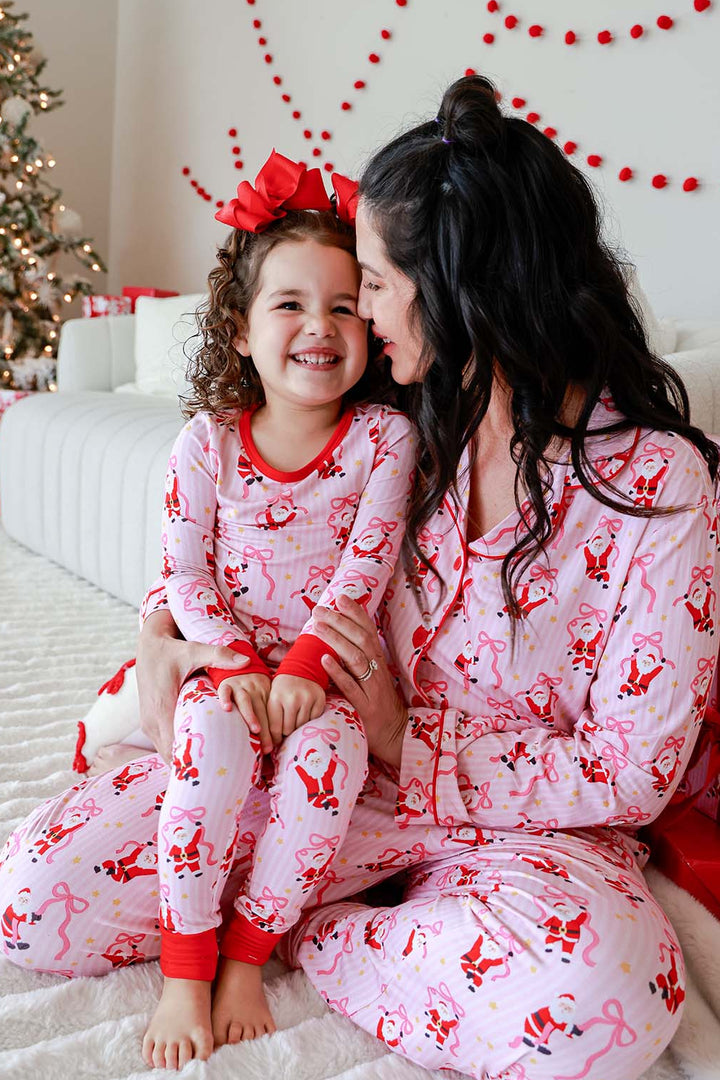 Mother and daughter wearing matching Caden Lane Jolly Ribbons Christmas bamboo pajamas, sharing a cozy holiday moment in festive Santa and ribbon bow prints.