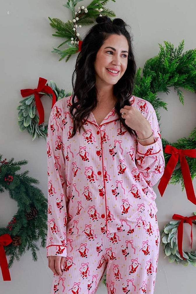 Woman modeling the Caden Lane Jolly Ribbons Women's Two-Piece Bamboo Christmas Pajama Set in front of festive holiday wreaths.