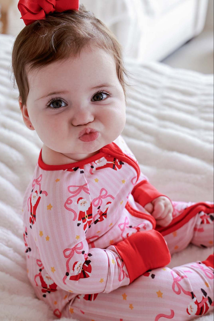 Baby wearing the Caden Lane Jolly Ribbons Christmas Bamboo Convertible Zip Romper featuring festive Santas and ribbon bows for a cozy holiday look.