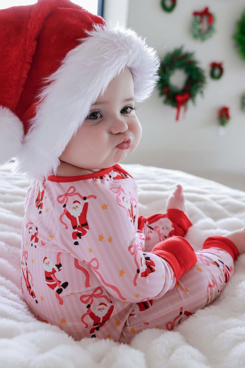 Baby wearing the Caden Lane Jolly Ribbons Christmas Bamboo Convertible Zip Romper with a festive Santa hat for cozy holiday photos.