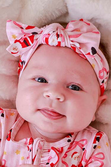 Baby wearing the Caden Lane Jolly Ribbons Christmas Knit Large Bow Headwrap featuring festive Santa and ribbon bow print, paired with a matching holiday outfit.