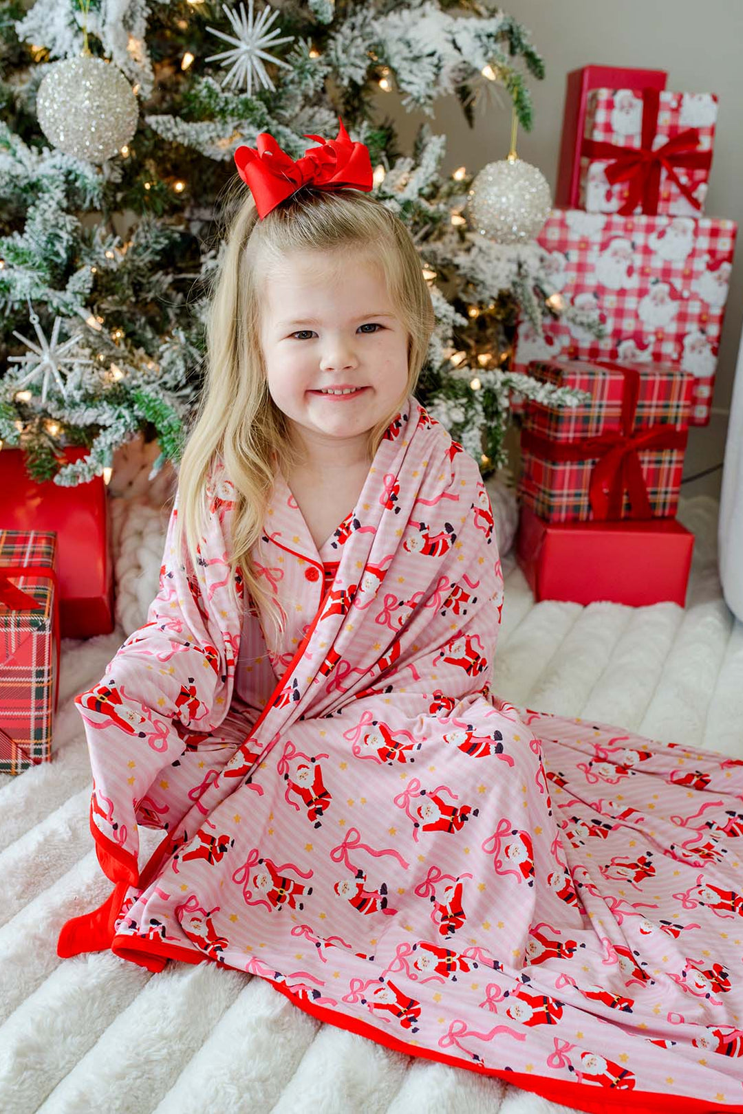 Caden Lane Personalized Name Christmas Blanket in the Jolly Ribbons print wrapped around a smiling child, featuring festive Santa and ribbon design, matching family Christmas pajamas, and personalized holiday keepsakes.