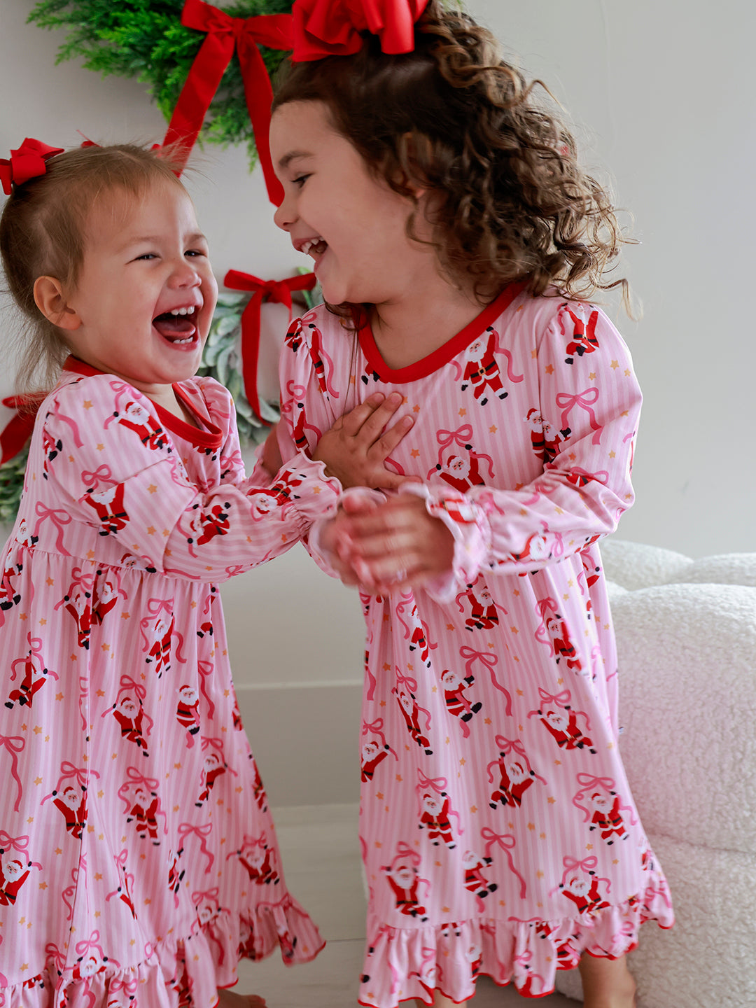 Sisters wearing matching Caden Lane Jolly Ribbons Girls' Long Sleeve Christmas Nightgowns featuring festive Santa and ribbon bow prints.