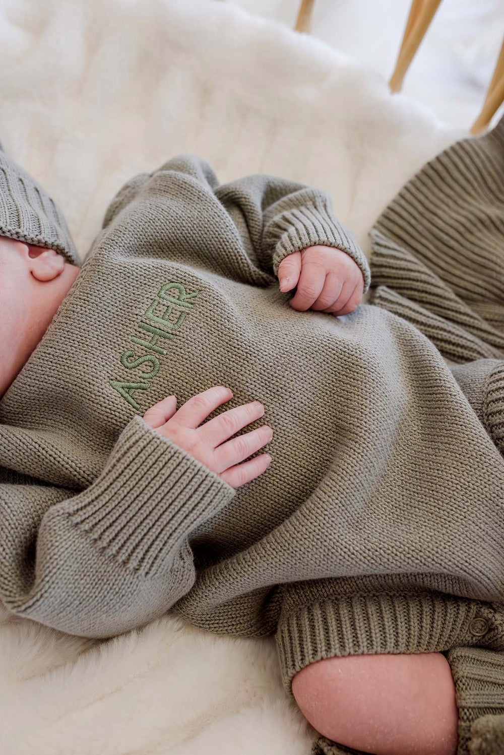 Baby snuggled in Caden Lane knit bubble outfit, hand resting on custom embroidered name "Asher" on smoke sweater romper