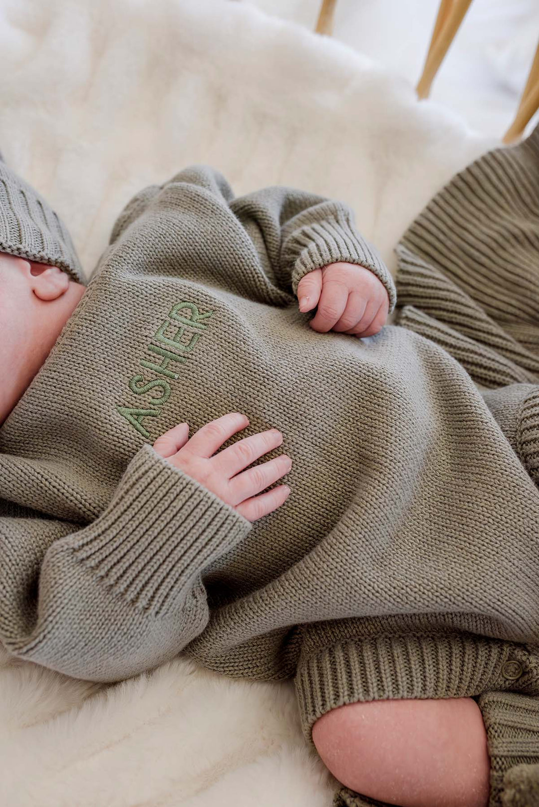 Baby snuggled in Caden Lane knit bubble outfit, hand resting on custom embroidered name "Asher" on smoke sweater romper