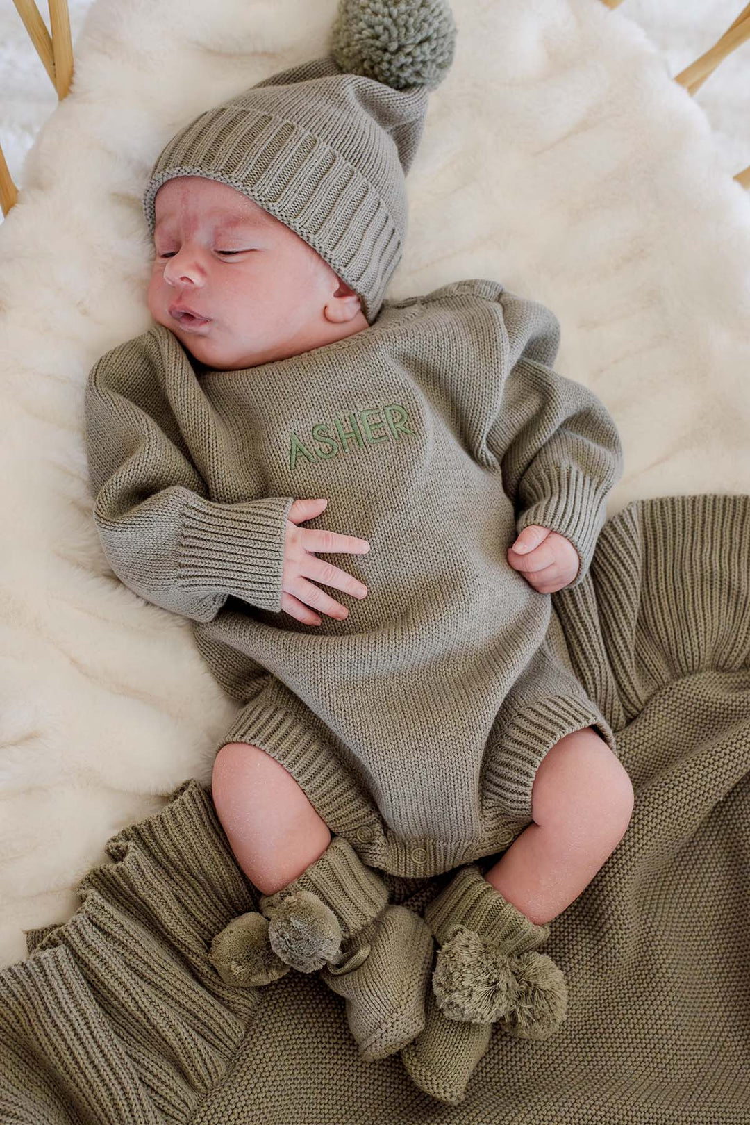 Newborn boy in Caden Lane smoke knit bubble romper, matching pom-pom hat, and personalized "Asher" embroidery