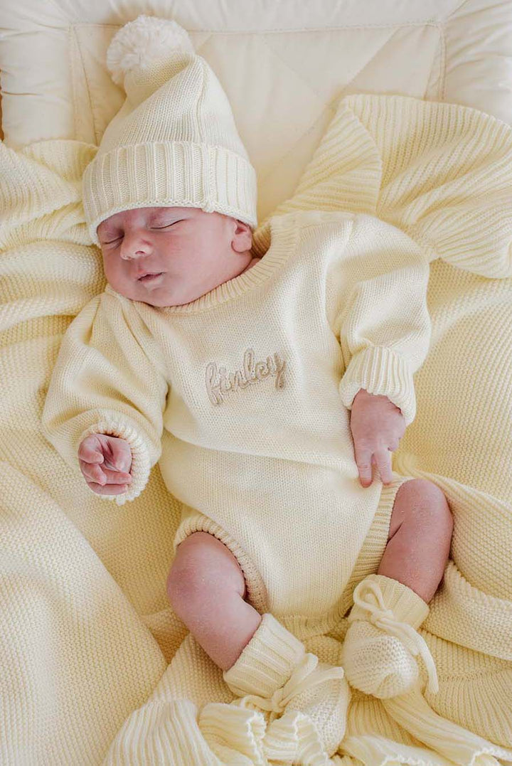 Newborn sleeping in Caden Lane ivory knit bubble romper and hat personalized with the name Finley
