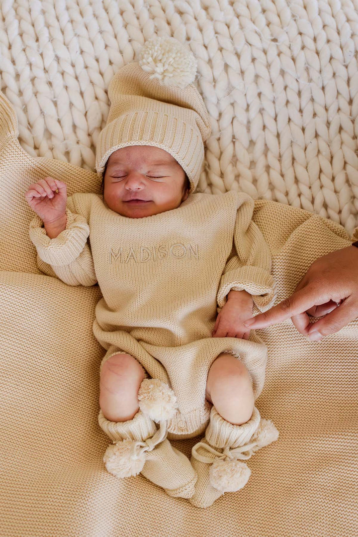 Smiling newborn in Caden Lane beige knit bubble romper and hat personalized with the name Madison