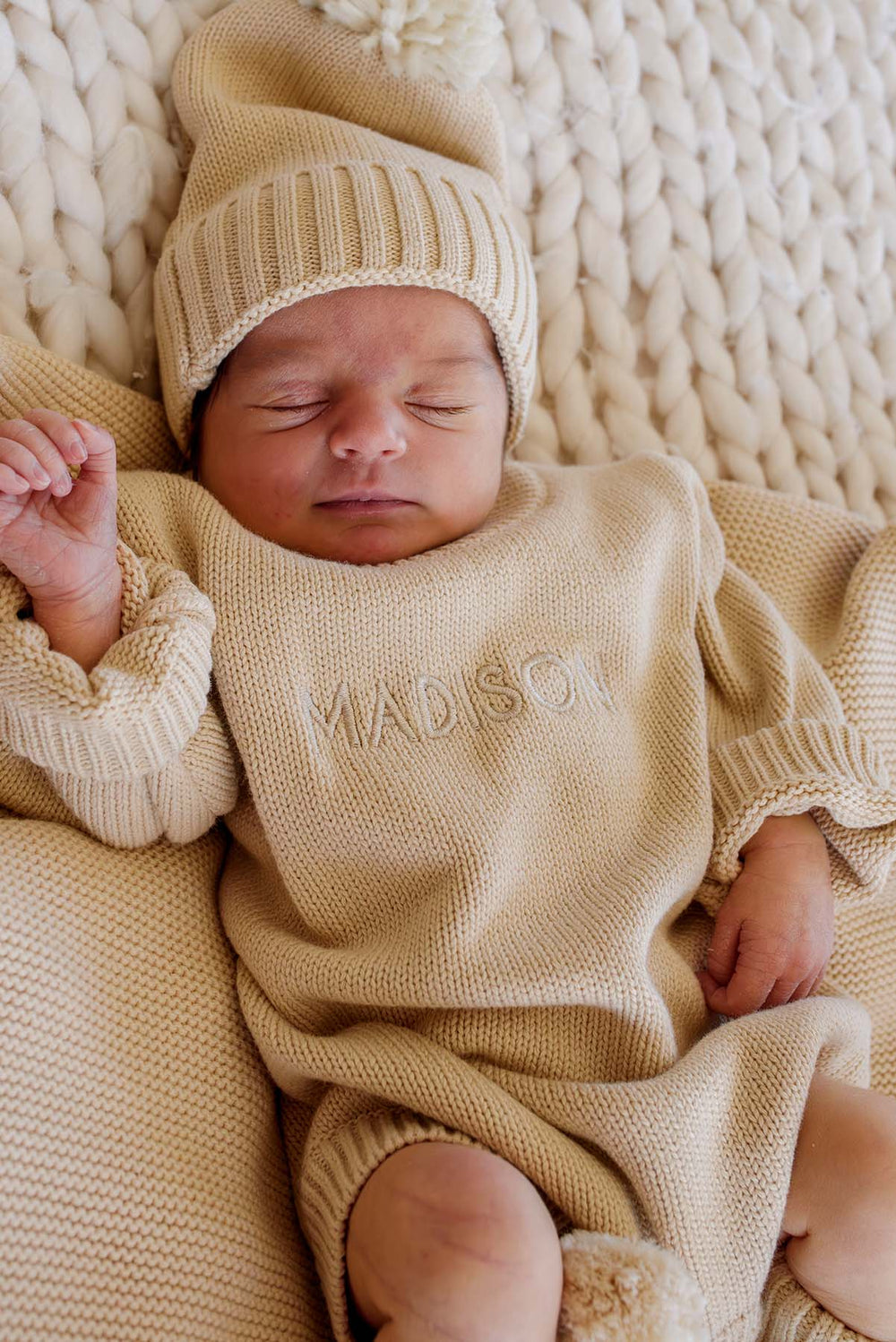 Baby's hand and feet in Caden Lane beige knit bubble romper with matching pom-pom booties, personalized name embroidery