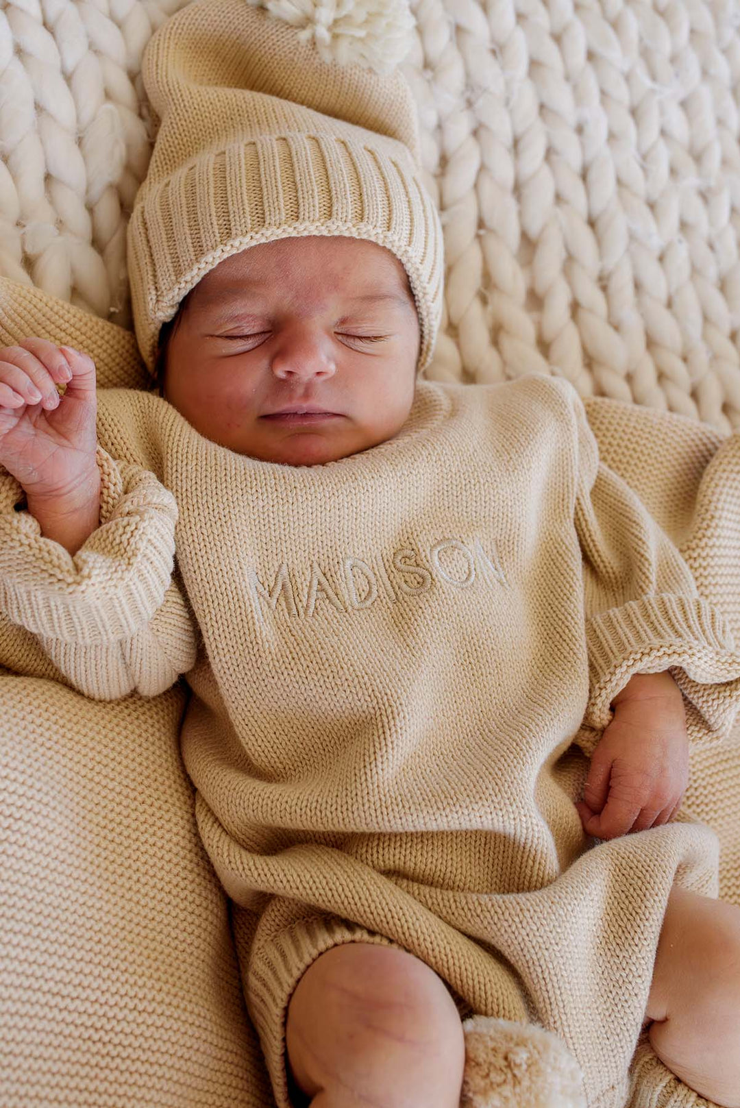 Baby's hand and feet in Caden Lane beige knit bubble romper with matching pom-pom booties, personalized name embroidery