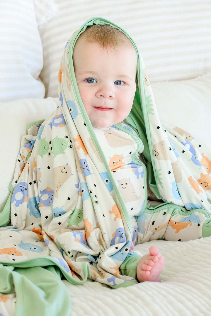 Baby wrapped in a Caden Lane sage green-trimmed Little Monsters bamboo blanket, wearing matching monster-print pajamas