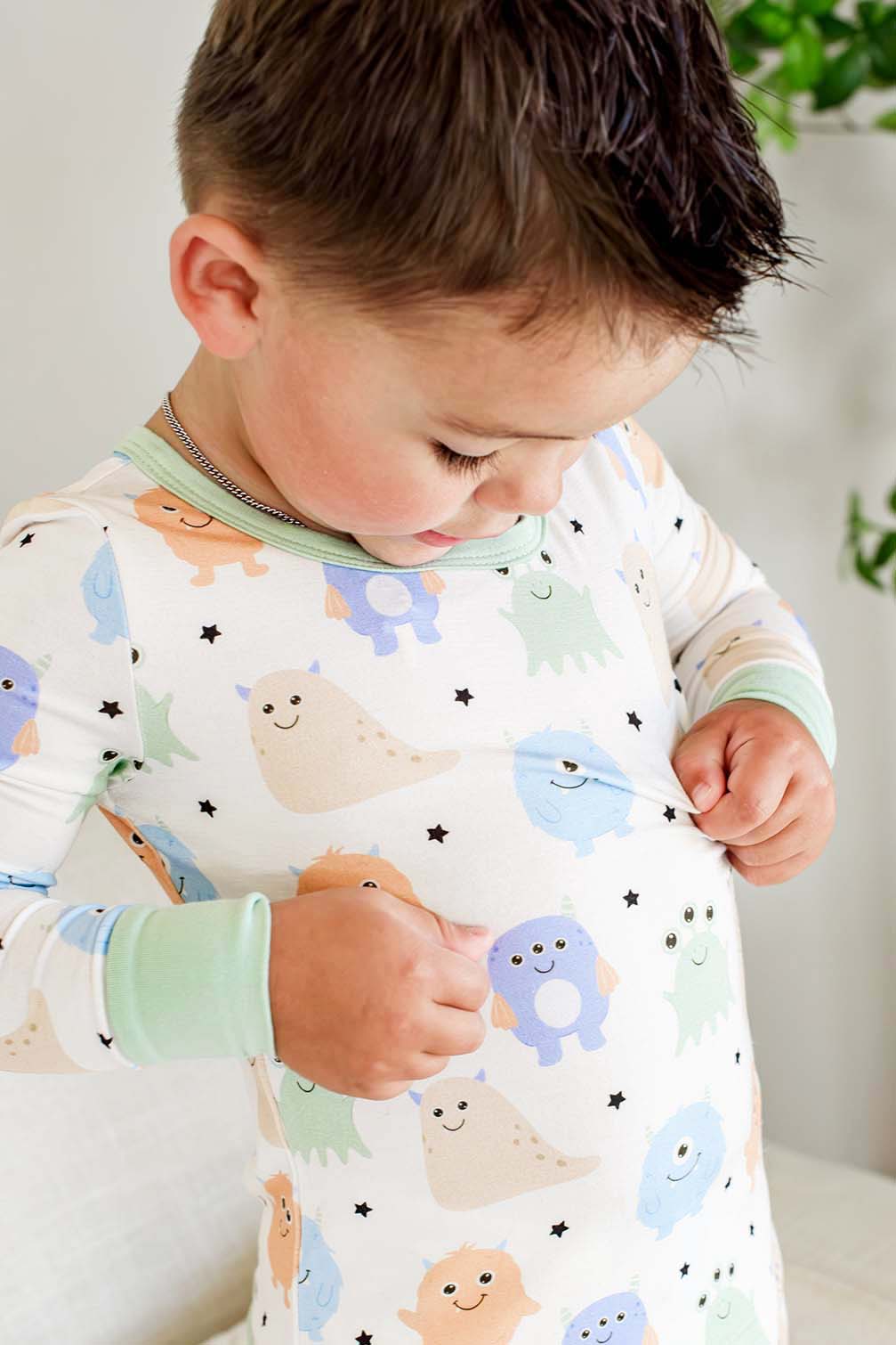 Close-up of a toddler's torso and neckline showing the print and sage green trim of a Caden Lane Little Monsters two-piece pajama set