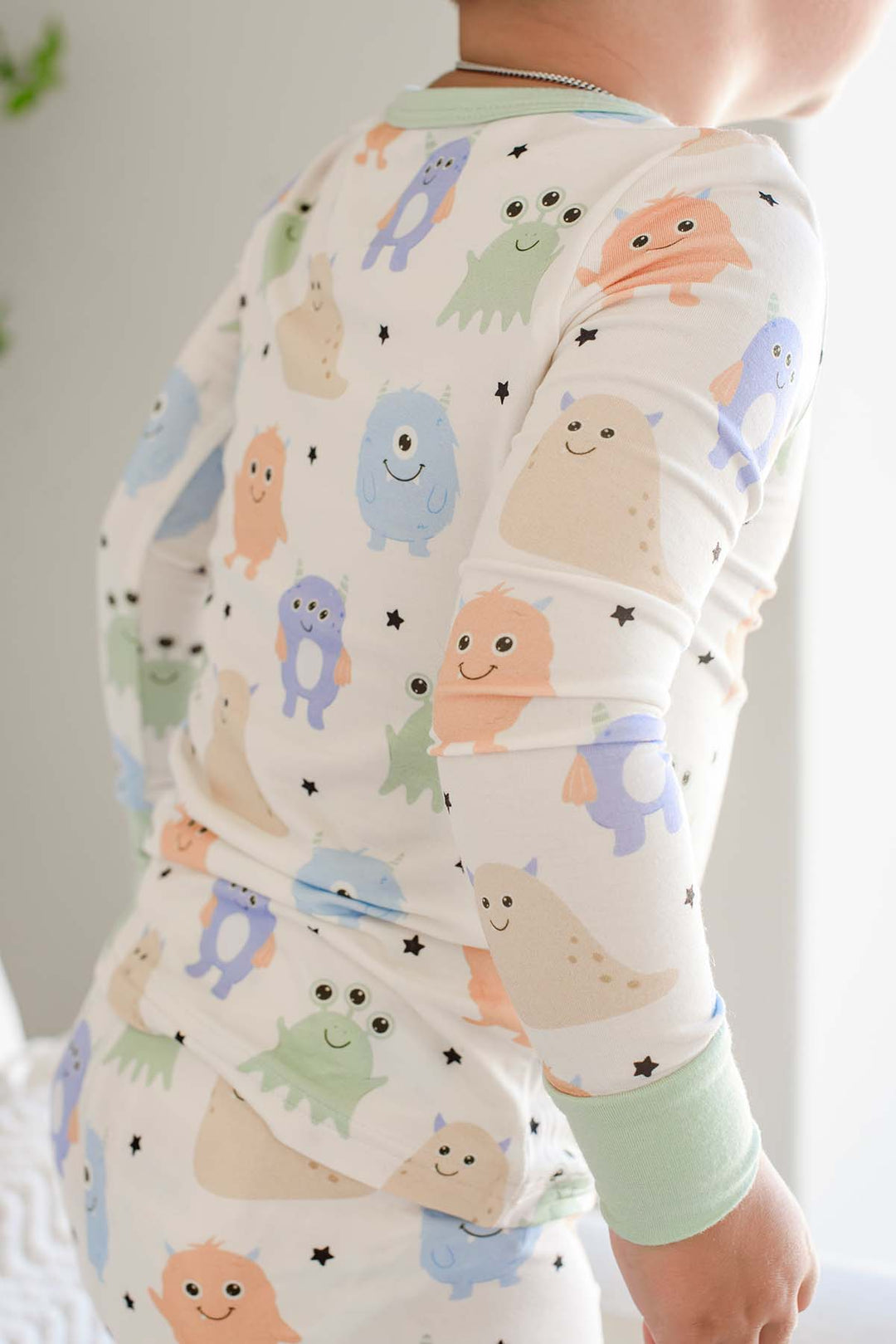 Close-up of a toddler's bak showing the monster print and sage green trim of a Caden Lane Little Monsters two-piece pajama set