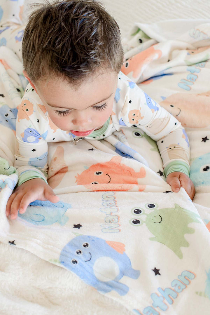 Close-up of a toddler boy in matching monster-print pajamas holding a Caden Lane personalized "Nathan" Little Monsters minky blanket