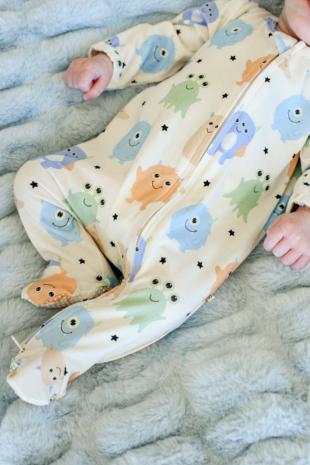Close-up of a newborn's legs and feet in a Caden Lane Little Monsters print footie, showing the zipper and footed detail