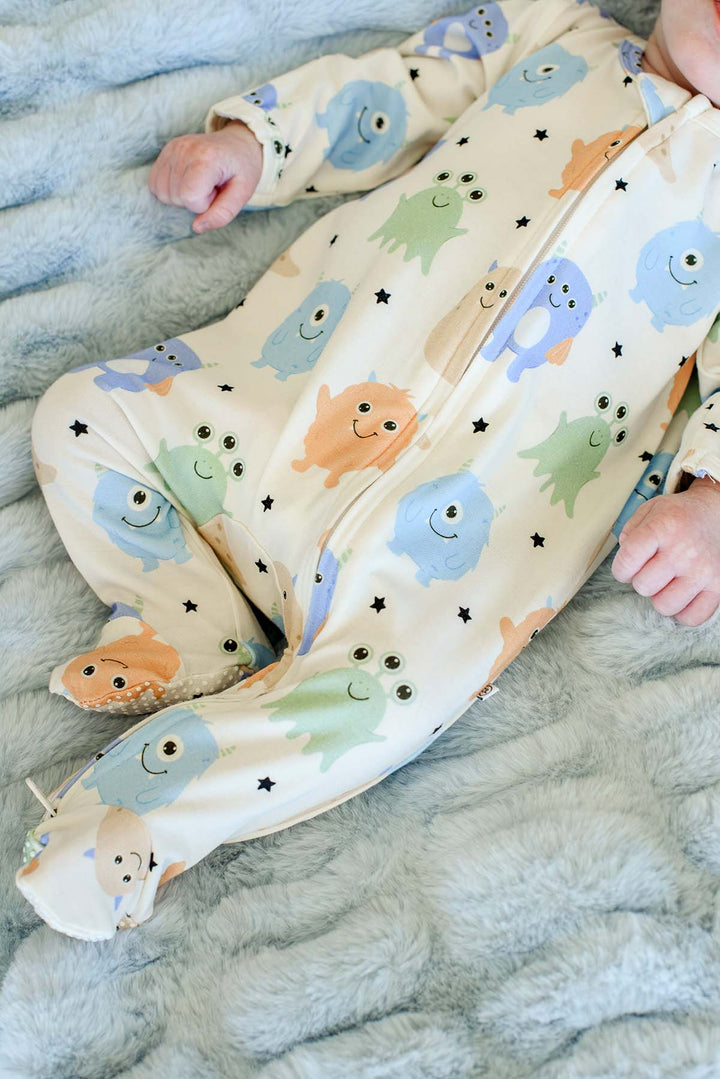 Close-up of a newborn's legs and feet in a Caden Lane Little Monsters print footie, showing the zipper and footed detail