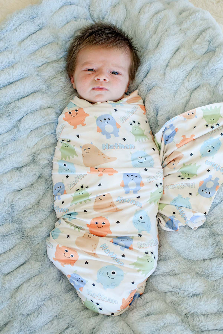 Newborn swaddled in Caden Lane personalized "Nathan" Little Monsters print blanket, close-up view on a blue faux fur blanket