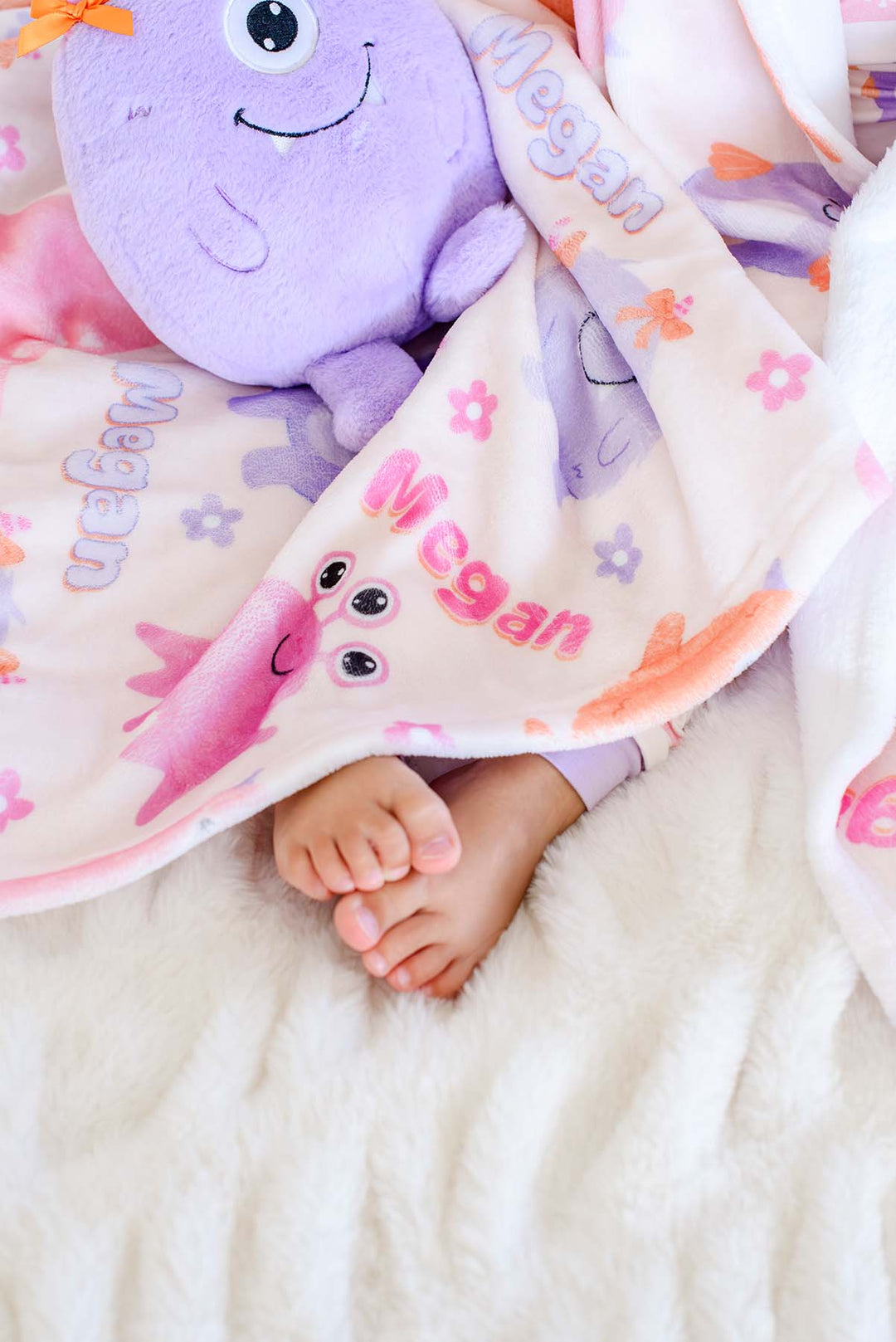 Close-up of a toddler's Caden Lane personalized "Megan" Little Monsters minky blanket with pink, purple, and orange cartoon monsters and flowers