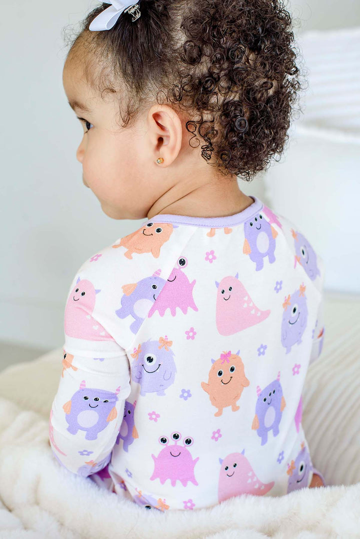 Close-up side/back view of a toddler's shoulder and neckline, showing print detail of a Caden Lane Little Monsters zipper footie with lavender trim