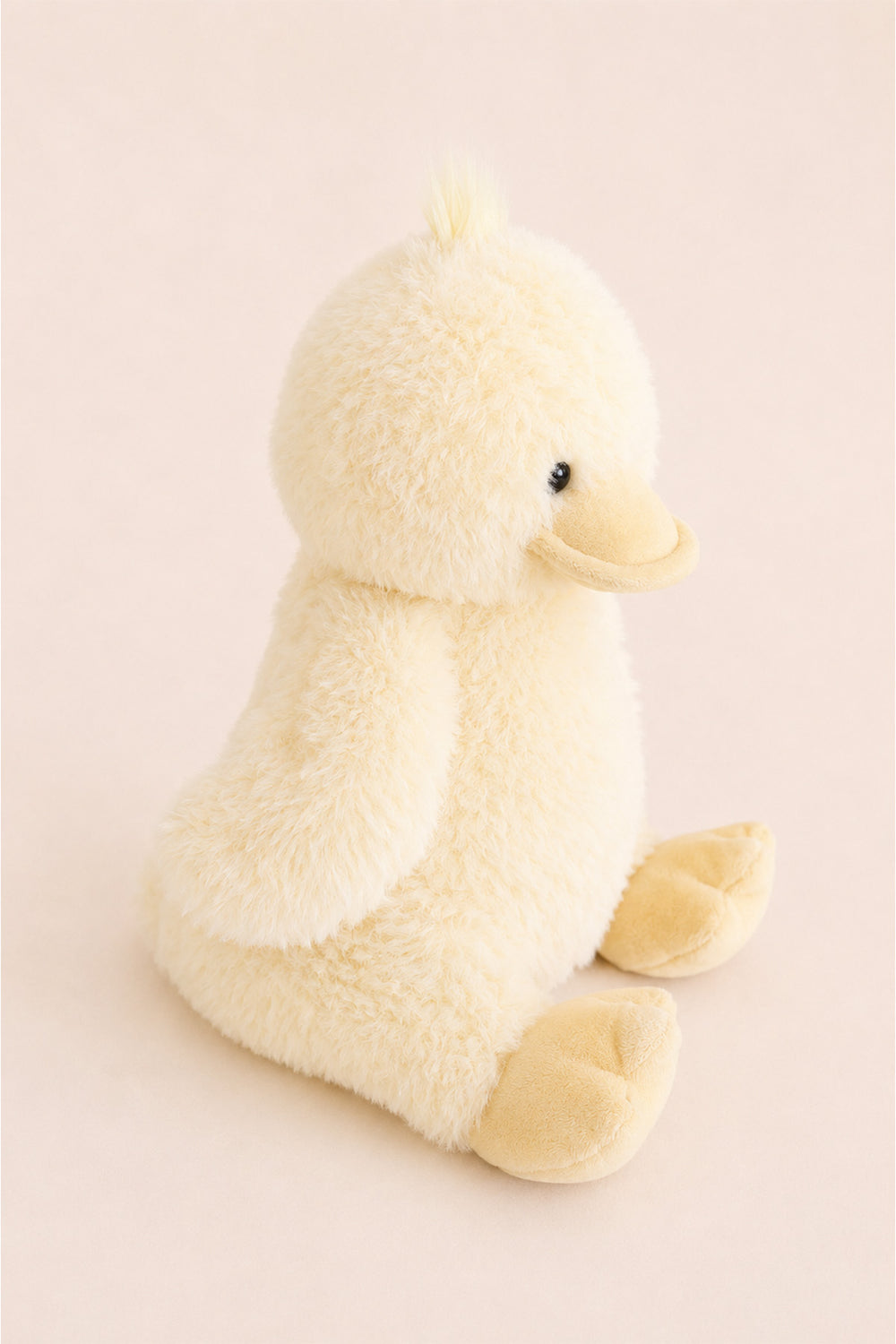 A Caden Lane plush yellow duck toy with a soft, fuzzy texture, sitting on a solid pale pink background.