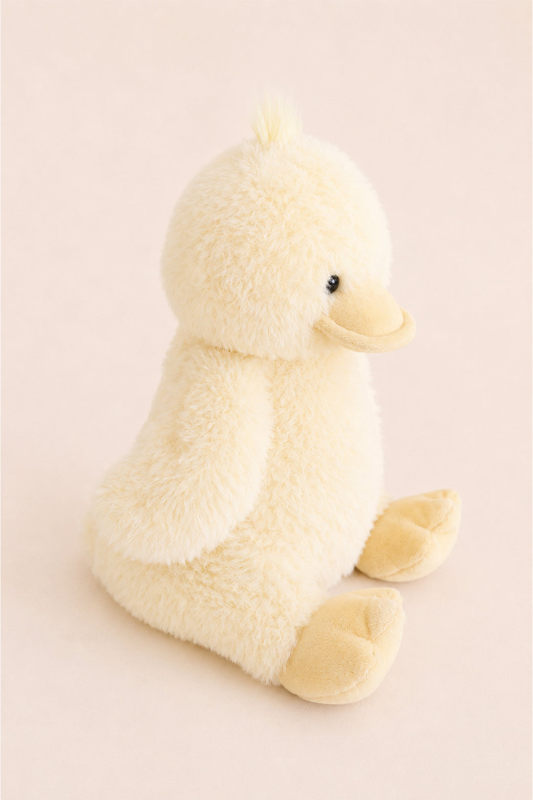 A Caden Lane plush yellow duck toy with a soft, fuzzy texture, sitting on a solid pale pink background.