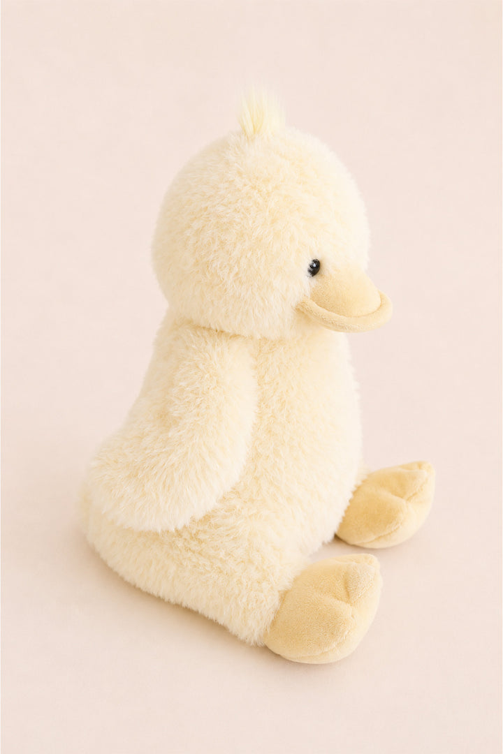 A Caden Lane plush yellow duck toy with a soft, fuzzy texture, sitting on a solid pale pink background.