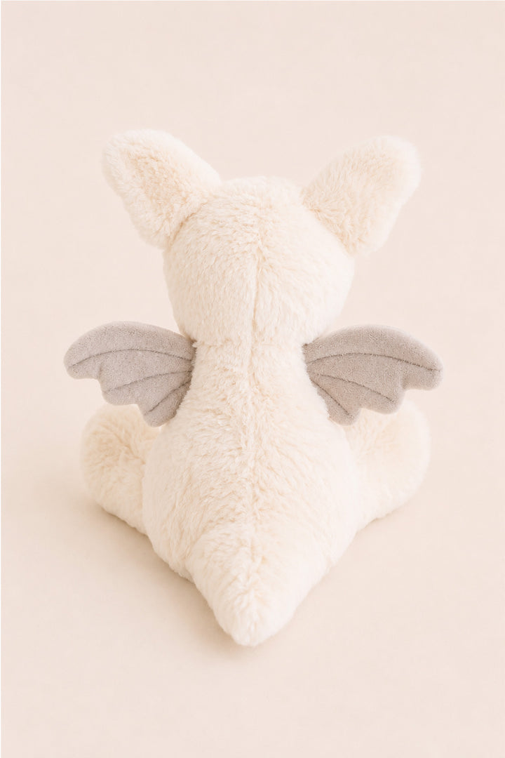 A Caden Lane plush toy dragon shown from the back, featuring fluffy cream-colored fur, small pointed ears, and soft gray wings, set against a solid pale beige background.