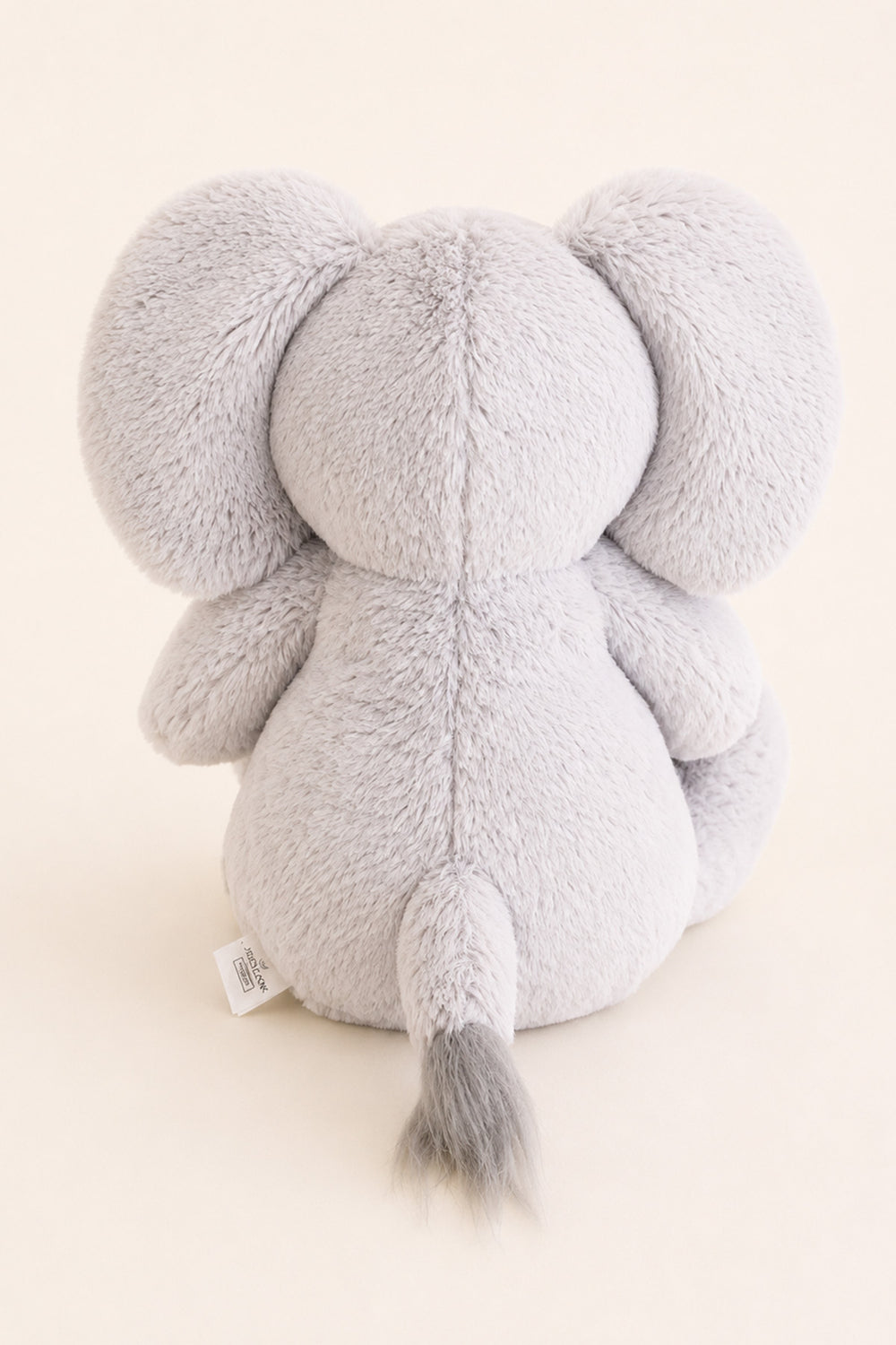 A lCaden Lane light gray plush elephant toy shown from the back, featuring soft textured fabric, large ears, and a small gray-tipped tail, photographed against a warm off-white background.