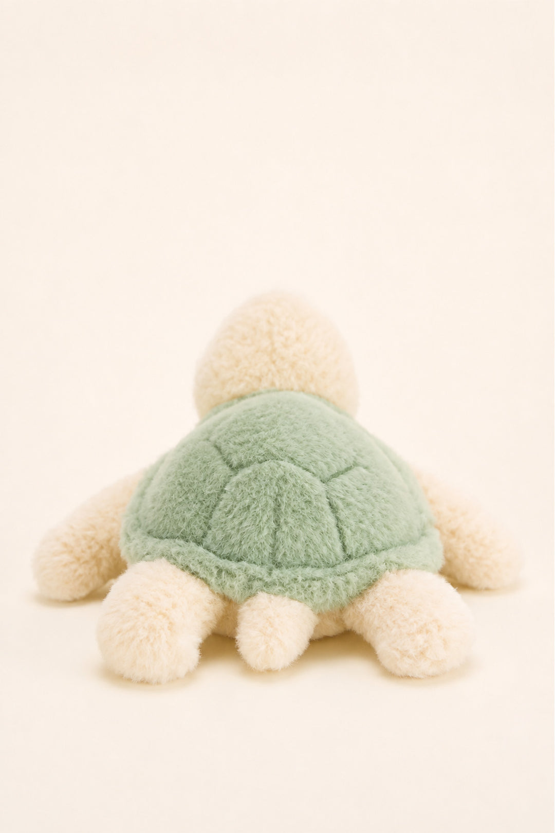 A Caden Lane plush turtle toy viewed from the back, featuring a soft sage green shell and cream-colored limbs and head, set against a solid cream background.
