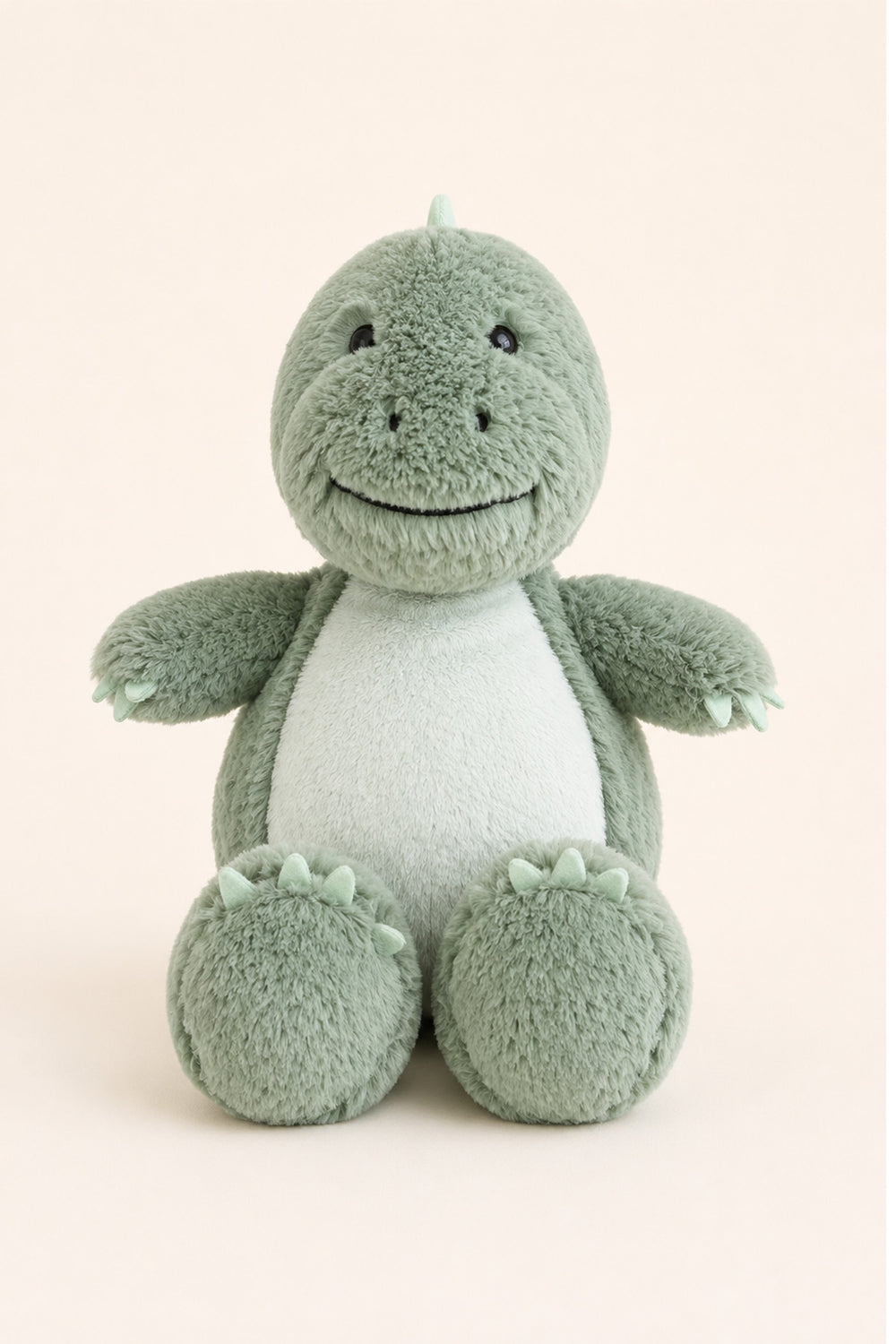 A plush Caden Lane dinosaur toy in sage green and white, sitting against a solid pale beige background.