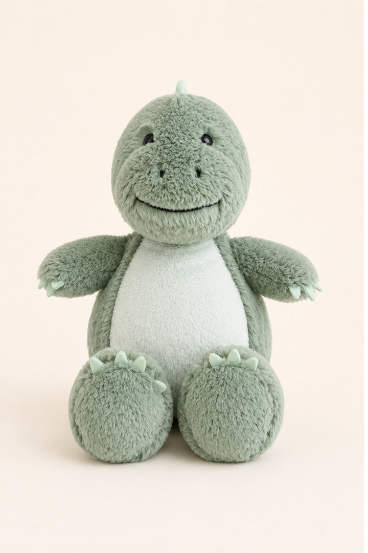 A plush Caden Lane dinosaur toy in sage green and white, sitting against a solid pale beige background.