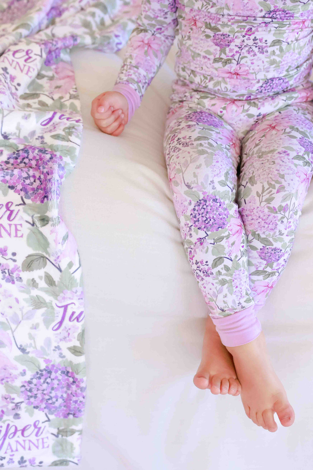 girl sitting on bed with legs crossed in lavender lullaby two piece pajama set