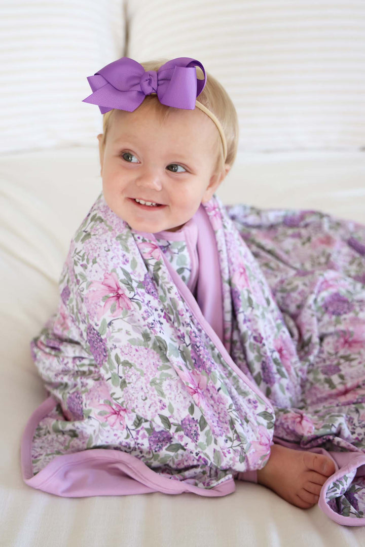 sitting baby girl looking over to the side with the lavender lullaby bamboo blanket wrapped around her shoulders 