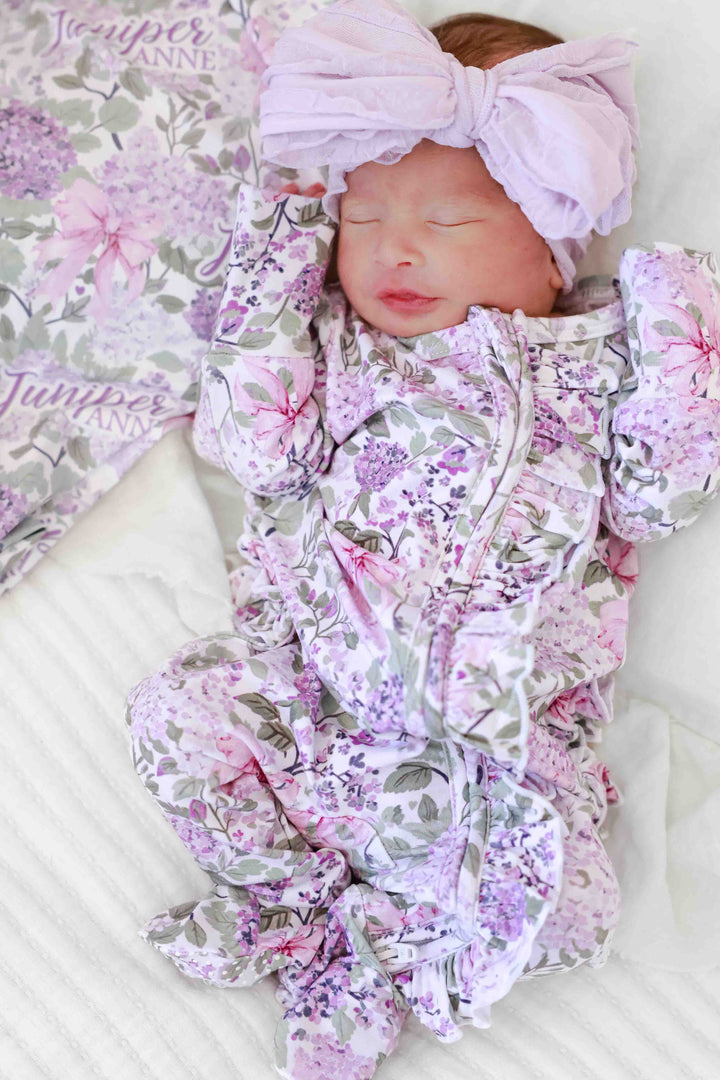 newborn girl in lavender lullaby ruffle zipper footie and purple ruffle knit bow