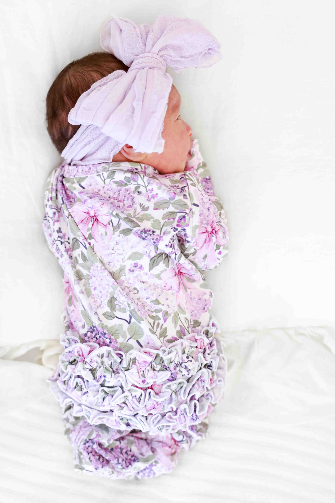 back view of ruffle bottom zipper footie in lavender lullaby print with matching purple ruffle bow