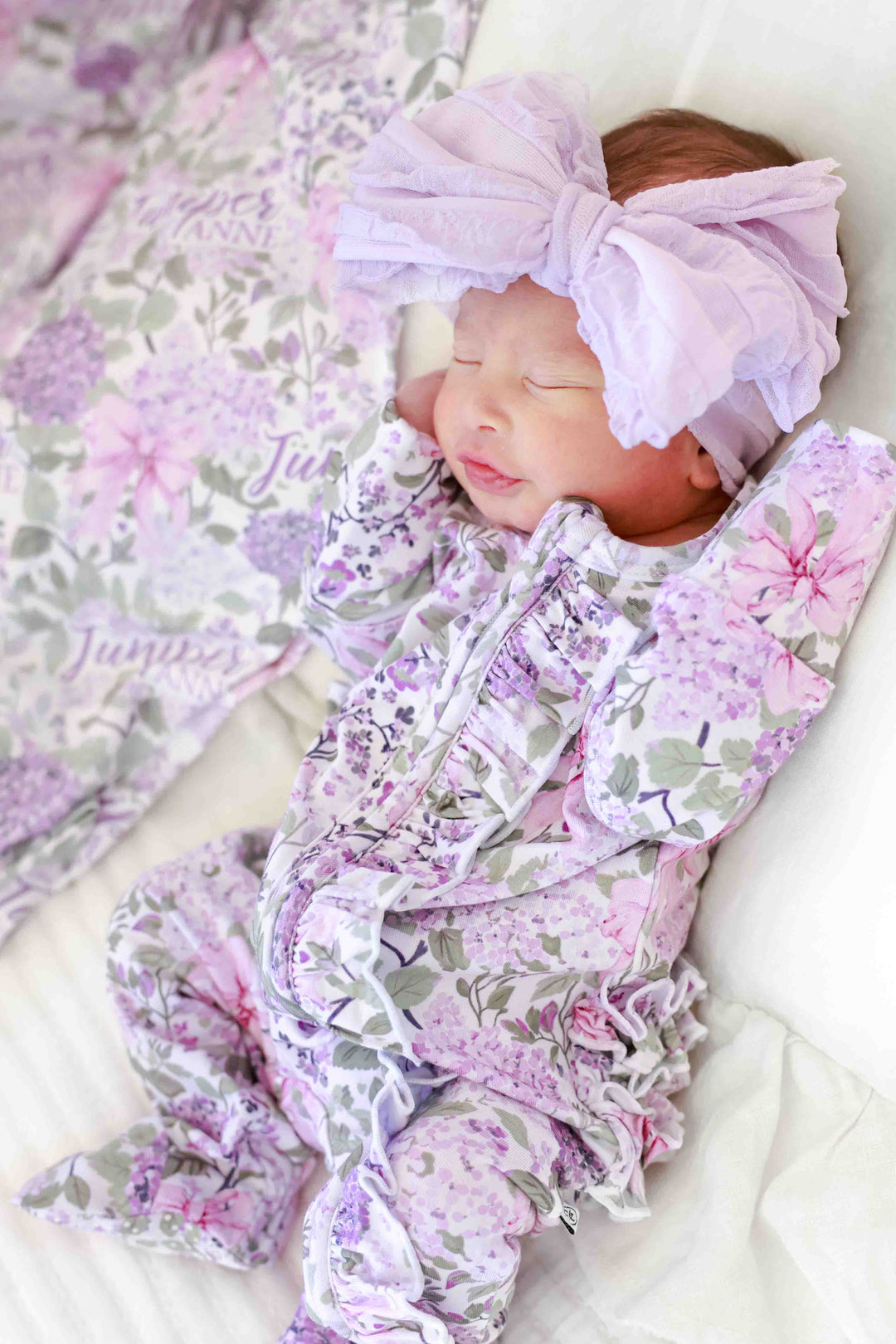 side view of lavender lullaby ruffle zipper footie for baby girl with a matching purple ruffle bow headwrap