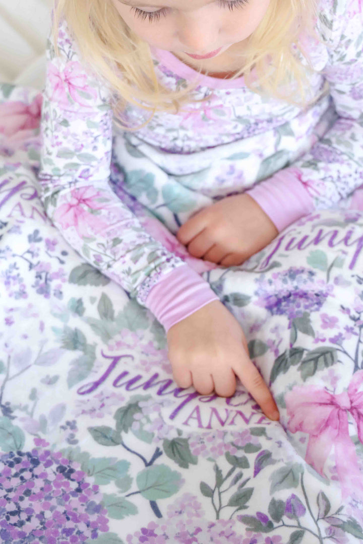girl point at name on lavender lullaby personalized blanket wearing matching pajamas 