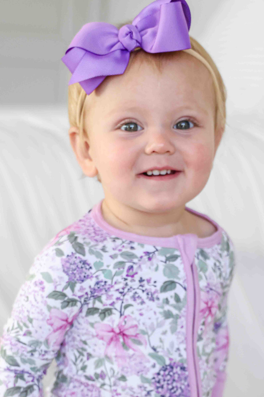 smiling baby girl wearing bright purple ribbon bow headband and lavender lullaby romper
