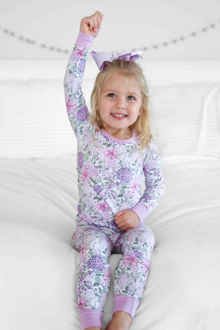 girl sitting on bed in lavender lullaby two piece pajama set