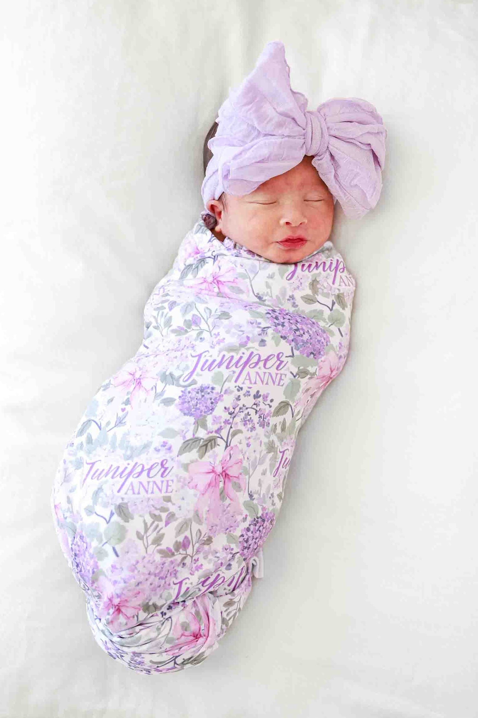 baby girl laying on pillow in lavender lullaby personalized swaddle with matching purple ruffle knit bow