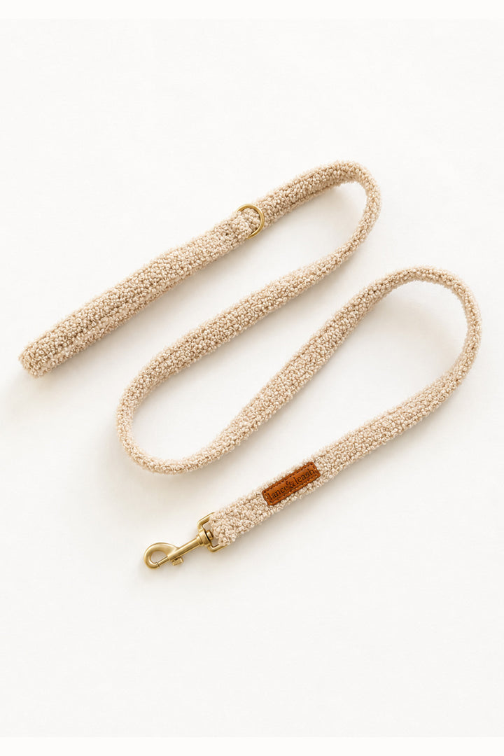 A Lane & Leash textured beige dog leash with a small brown leather brand patch and gold-tone hardware, laid out on a clean white background.