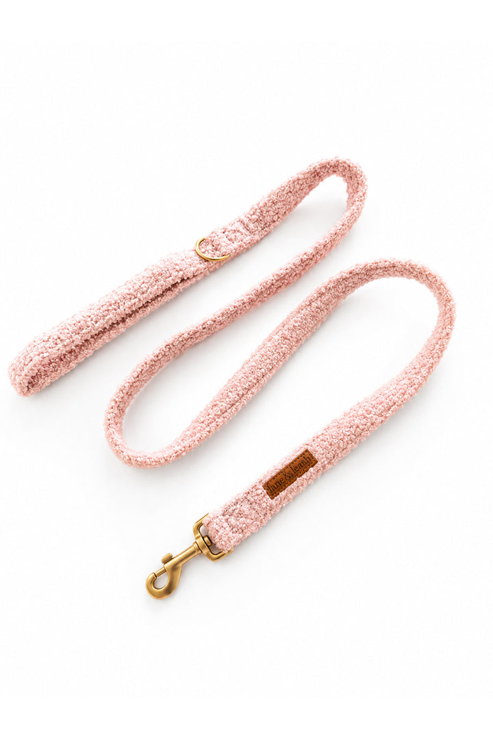 A Lane & Leash  light pink bouclé dog leash with a gold-tone metal clasp and a small brown leather brand patch, displayed on a clean white background.