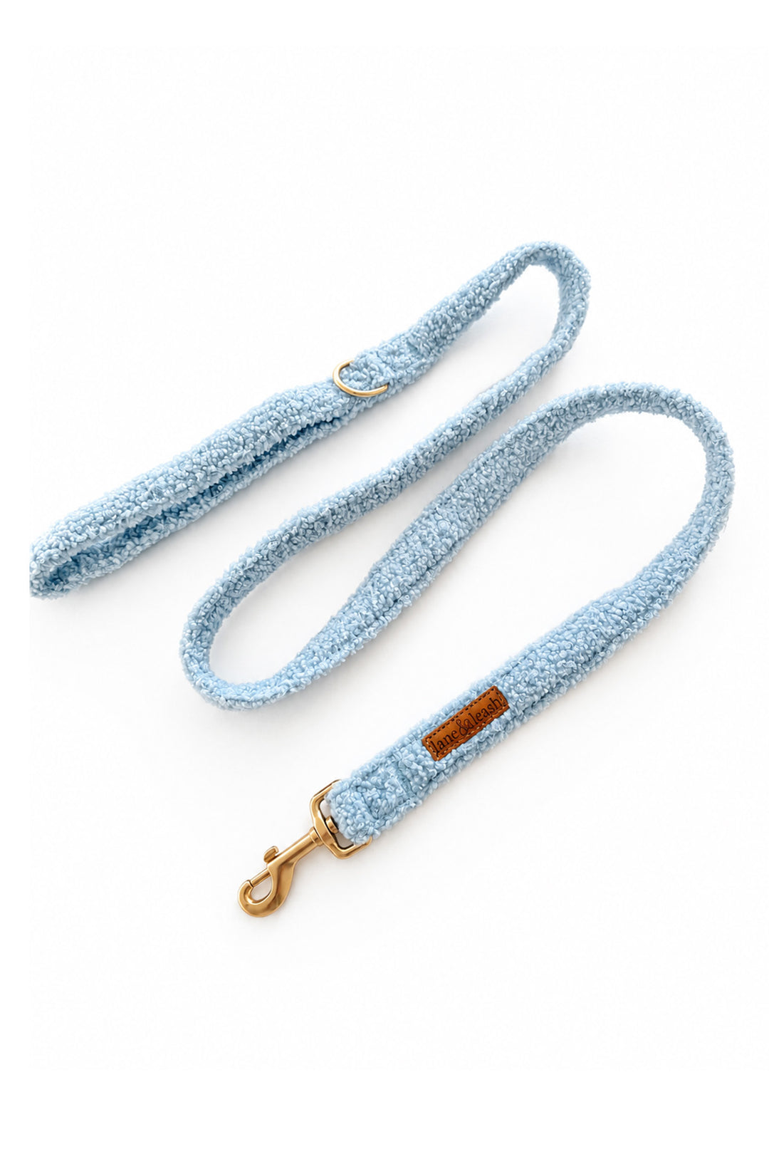 A Lane & Leash light blue textured fabric dog leash with gold-tone hardware, including a snap hook clasp and a small brown leather brand patch, displayed on a clean white background.